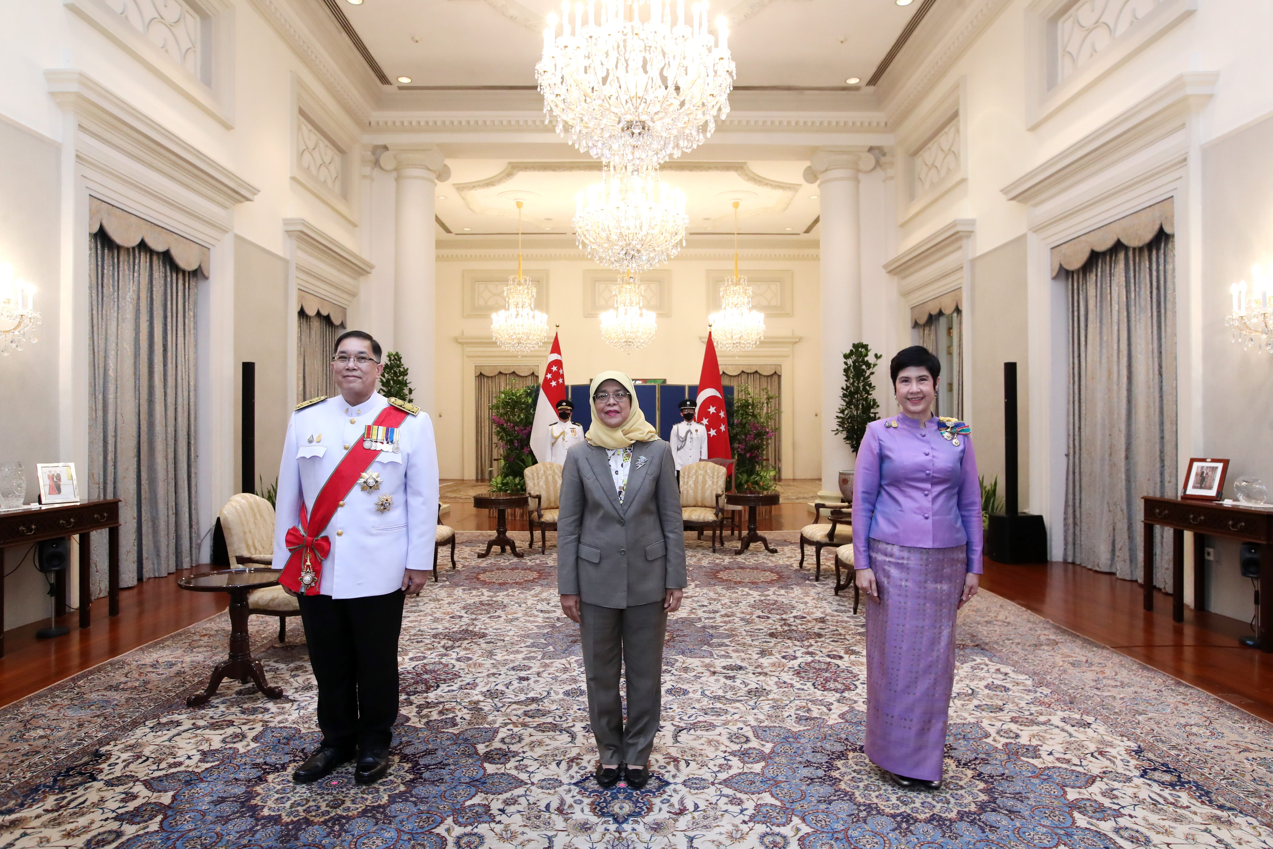 Halimah Yacob with two officials stand in front of Singapore flags in ornate room.